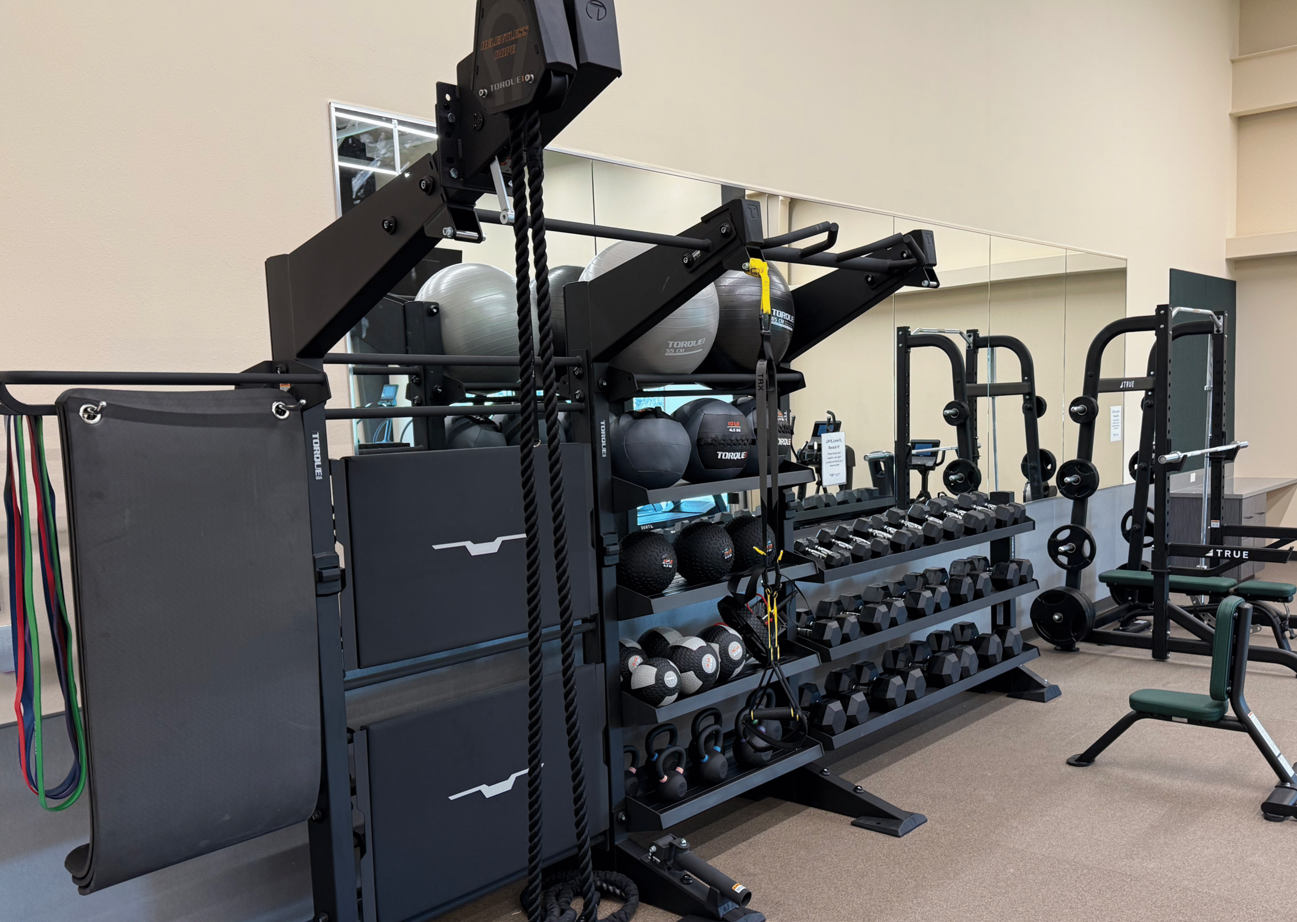 Strength Equipment Maintenance and Organization A neatly arranged gym space with functional training gear, dumbbells, and resistance tools from Torque and TRUE. The photo highlights the results of consistent maintenance and inspection — a clean, efficient, and high-performing fitness environment for users.