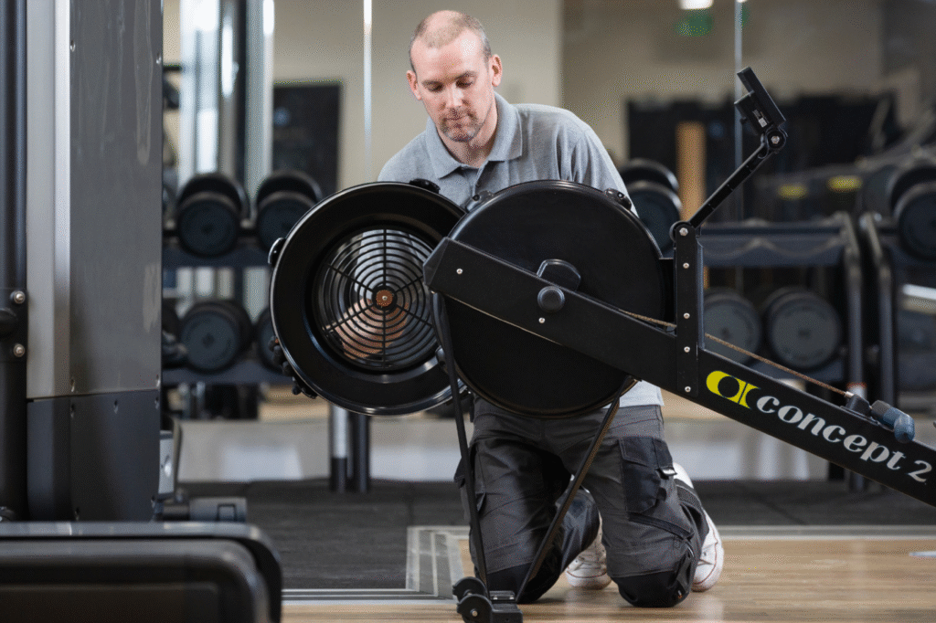 Technician performing maintenance on commercial fitness equipment in a gym.